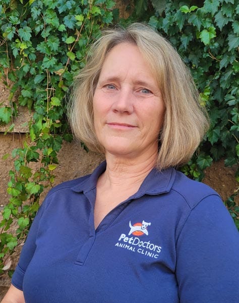A woman in a blue "Pet Doctors Animal Clinic" shirt stands outside in front of a wall covered with green ivy.