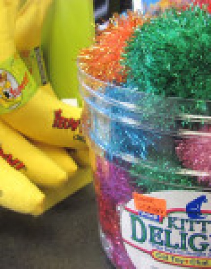 A jar of colorful sparkly pom-poms labeled "Kitty Delight" next to a display of yellow banana-shaped cat toys.