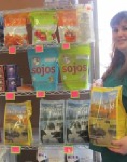 A woman stands beside shelves stocked with various pet food bags. She holds one of the bags while smiling.