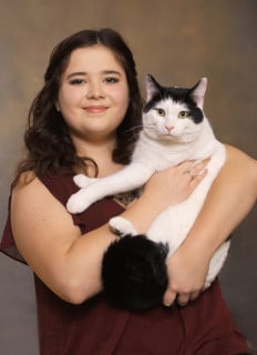 A person with long hair holds a large black and white cat against a plain background.